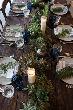 the table is set with plates, candles and greenery