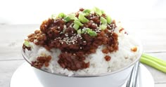 a white bowl filled with rice and meat on top of a plate next to a fork