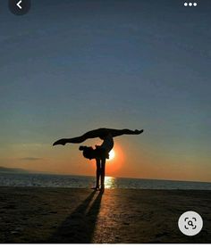 a person doing a handstand on the beach with the sun setting in the background