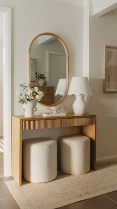 a white vase sitting on top of a table next to a mirror and stools