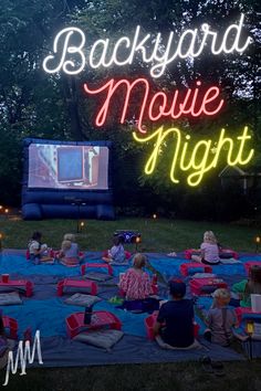 people sitting on blankets in front of a movie screen at night with the words backyard movie night lit up