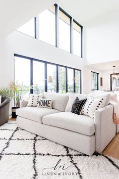 a living room filled with white furniture and large windows on top of the wall next to a rug