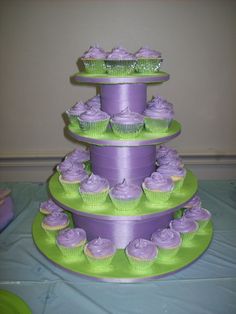 three tiered cake with cupcakes on the top and purple frosting on the bottom