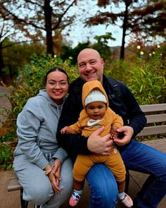 a man and woman sitting on a bench with a baby in their lap, smiling at the camera