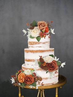 a three tiered cake with flowers and leaves on the top is sitting on a gold stand