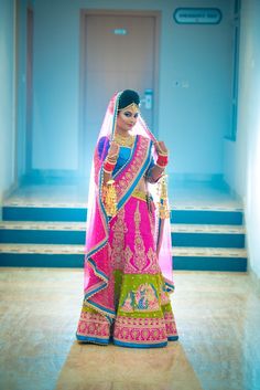 a woman in a pink and green bridal gown standing on steps with her hands behind her head