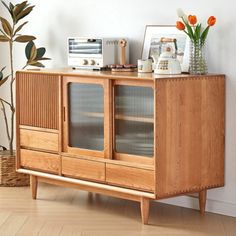 a wooden cabinet with glass doors and flowers in vases next to it on top of a hard wood floor