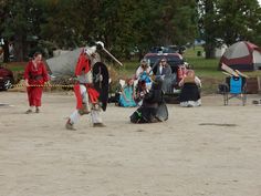 two men in costume are playing baseball on the field with tents and campers behind them