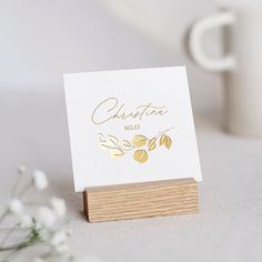 a white card sitting on top of a wooden stand next to a cup and flowers