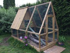 a small wooden chicken coop in the middle of some grass and flowers, with an open roof