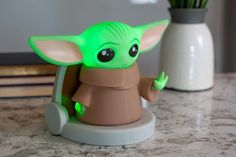 a small green toy sitting on top of a counter next to a vase with flowers