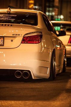 the back end of a white car parked in a parking lot at night with other cars behind it