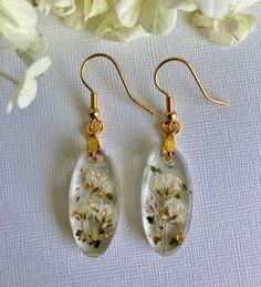 Discover the charm of nature with these handmade earrings, featuring real pressed Baby's Breath flowers encased in clear UV resin. Accented with tiny pieces of gold metal leaf, these lightweight earrings sparkle delicately, adding a touch of elegance to your look. Each flower tells a story. Baby's Breath symbolizes everlasting love, making these delicate earrings a truly meaningful gift. Whether for a baby shower, as bridesmaids' gifts, or a special surprise for a mom, these earrings convey deep Botanical Pressed Flower Wedding Jewelry, Delicate Oval Pressed Flower Jewelry, Delicate Oval Jewelry With Pressed Flowers, Dainty Flower Earrings With Birth Flower For Her, Delicate Handmade Earrings For Bridesmaids, Dainty Birth Flower Earrings As Gift For Her, White Pressed Flower Earrings For Wedding, White Flower Earrings With Pressed Flowers For Wedding, Dainty Birth Flower Earrings For Gift