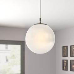 a white light hanging from the ceiling in a room with pictures on the wall behind it