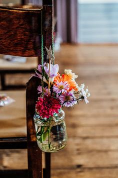 a vase filled with colorful flowers hanging from a wooden church pew, next to an empty chair