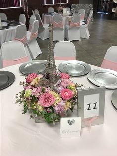 the table is set with plates, silverware and pink flowers in front of the eiffel tower