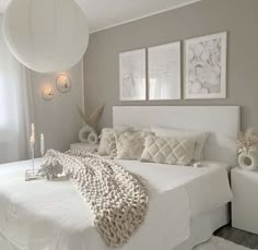 a white bed sitting in a bedroom next to two candles and pictures on the wall