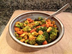 a bowl filled with broccoli and carrots on top of a wooden cutting board