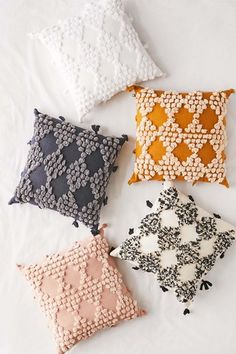 four different colored pillows sitting on top of a white bed sheet with black and white designs