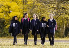 four girls in school uniforms walking through the grass