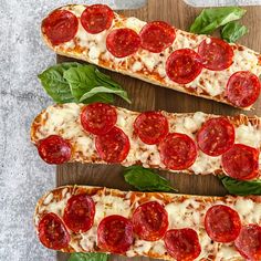 three slices of pizza with pepperoni and spinach leaves on a wooden cutting board