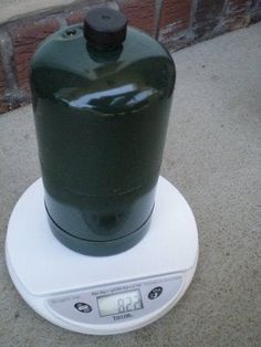 a large green jug sitting on top of a white digital scale in front of a brick wall