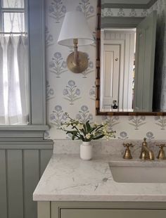 a white sink sitting under a bathroom mirror next to a counter with flowers in it