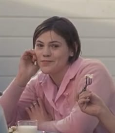 two women sitting at a table eating food and talking on their cell phones while one woman holds a fork in her hand