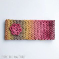 a crocheted headband with a pink flower on the front and yellow, brown, and orange stripes behind it