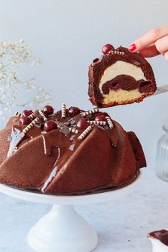 a person holding a piece of cake with chocolate frosting and cherries on it