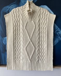 a white knitted sweater hanging on a wall next to a blue and white painting