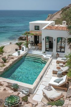 an outdoor swimming pool next to the ocean with lounge chairs around it and plants growing on the rocks