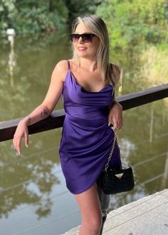 a woman in a purple dress leaning on a rail next to a body of water