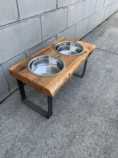 two stainless steel bowls sit on a wooden table with black metal legs, against a gray brick wall