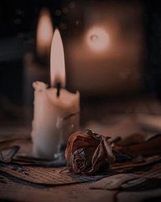 two white candles with one candle lit and the other on top of some cloths