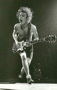 a shirtless man playing an electric guitar in the rain with his mouth wide open