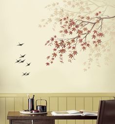 birds flying in the air over a wooden table and wall with red leaves on it