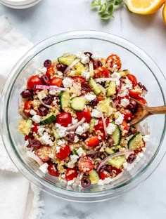 a salad in a glass bowl on top of a table with lemons and other ingredients