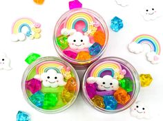 three small jars filled with colorful candies on top of a white table next to rainbows and clouds