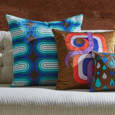 four decorative pillows on a couch in front of a brown brick wall with blue, green and red designs