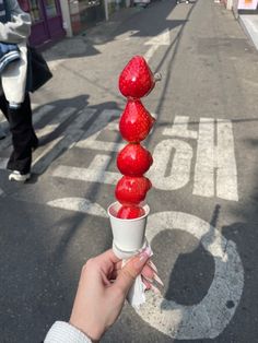 a person is holding an ice cream cone with strawberries on it in the street