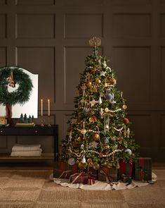 a christmas tree with presents under it in front of a mirror and wreath on the wall