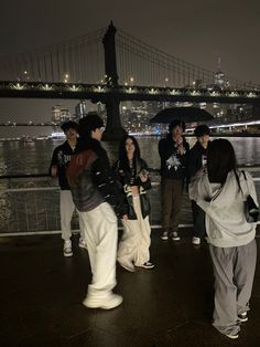 a group of people standing next to each other under an umbrella near the water at night