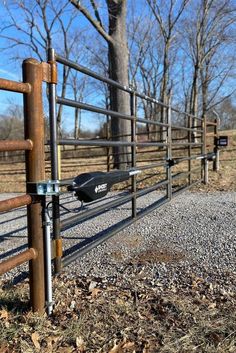 a metal fence that is next to a dirt road with trees in the back ground