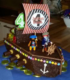 a cake shaped like a pirate ship with figures on the front and sides, sitting on top of a blue table cloth