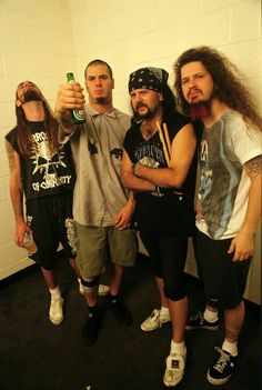 three men standing next to each other in a room with one holding a beer bottle