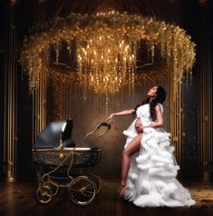 a woman in a white dress is sitting next to a baby carriage and gold chandelier