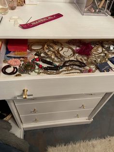 the drawer is full of jewelry and bracelets on it's side, which sits atop a white table