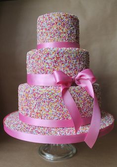 a three tiered cake with pink ribbon and sprinkles