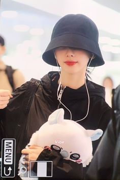 a woman wearing a black hat and holding a stuffed animal in her hand while walking through an airport